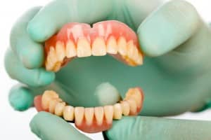 Gloved hand holding dentures, Foundations of Health Dental Care, Dentist St. Joseph, MO