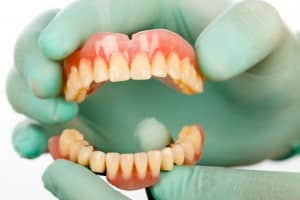 Gloved hand holding dentures, Foundations of Health Dental Care, Dentist St. Joseph, MO